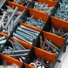 Pojemnik z przegródkami pełen śrub, kołków do regipsu metalowych i innych elementów złącznych.