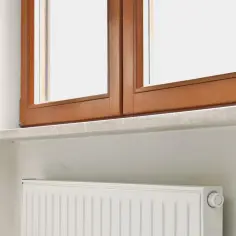 Drewniane okno, kamienny parapet i biały grzejnik. Idealne miejsce, by zastanowić się, kiedy montować parapety wewnętrzne.