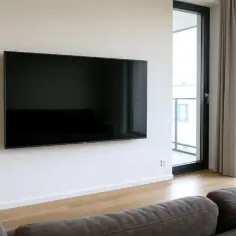 Nowoczesny salon z dużym telewizorem na ścianie. Idealna wysokość, by wygodnie oglądać filmy z kanapy. Jak wysoko wieszać tv? Tu jest przykład.