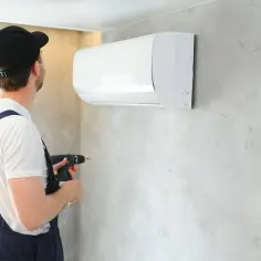 Fachowiec montuje instalację klimatyzacji w mieszkaniu, używając wiertarki.