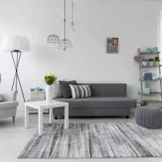 Jasny salon z szarą kanapą i fotelem. Inspiracja, jak pomalować ściany w salonie, by uzyskać taki efekt.