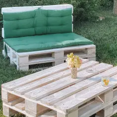 Stół z palet do ogrodu, z wygodną kanapą i stolikiem kawowym, ozdobiony kwiatami i świecami.