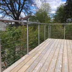 Nowoczesne mocowanie balustrady do czoła balkonu z drewna. Stalowe słupki i linki tworzą bezpieczne i estetyczne zabezpieczenie.