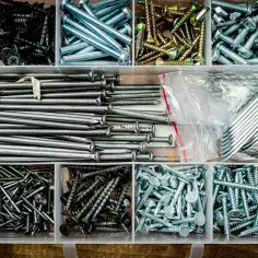 Pudełko z narzędziami pełne gwoździ do drewna, śrub i metalowych kątowników.