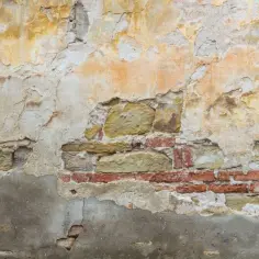 Odkryta cegła i kamień w zniszczonym tynku to sygnał, że trzeba pomyśleć, jak naprawić odpadający tynk zewnętrzny.