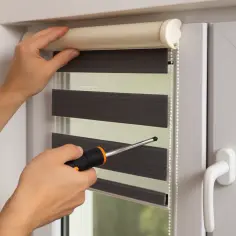 Montaż rolety dzień noc. Ręce przykręcają mechanizm do okna.