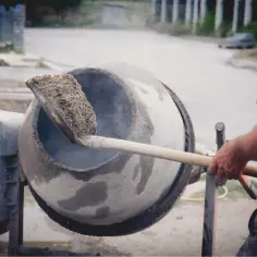 Mężczyzna wsypuje łopatą materiał do betoniarki, z której unosi się para.