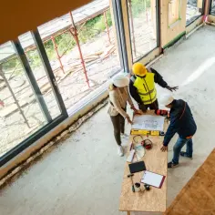 Architekci omawiają projekt domu, zastanawiając się, ile kosztuje tynkowanie domu. Na stole plany, próbki kolorów i narzędzia.
