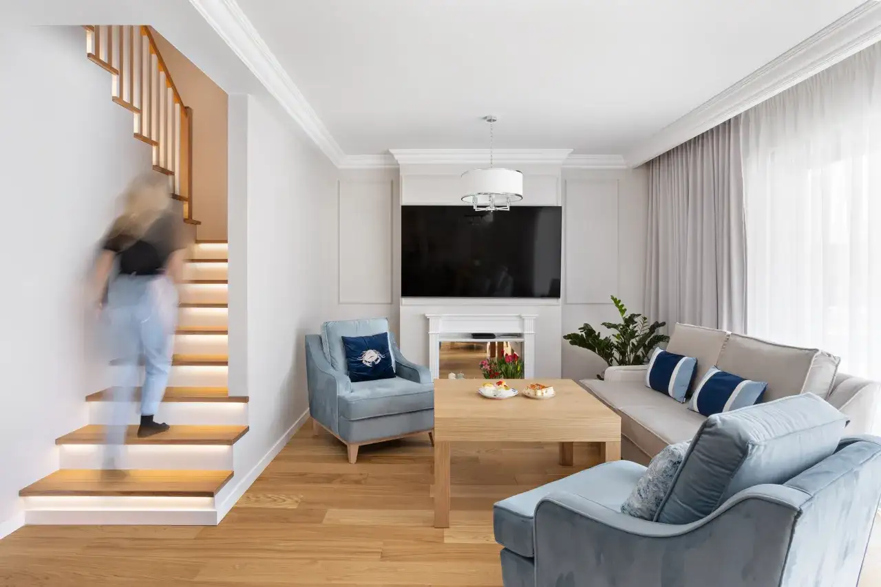 Nowoczesny salon z podświetlanymi schodami, idealny przykład jak urządzić salon. Jasne meble, pastelowe akcenty i drewno tworzą przytulną atmosferę.