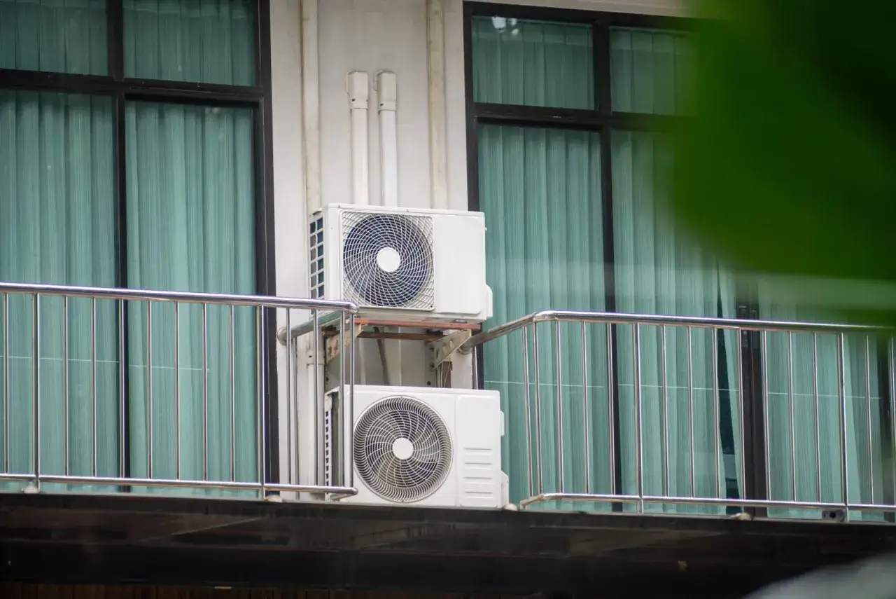 Montaż klimatyzacji w mieszkaniu. Dwa białe urządzenia zamontowane na ścianie budynku, za metalową balustradą.