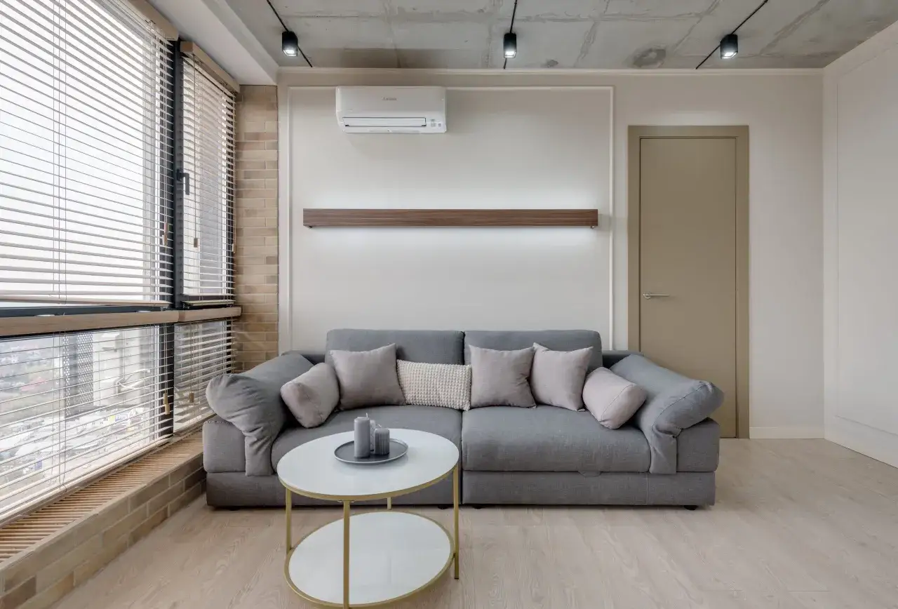 Nowoczesny salon z szarą kanapą, stolikiem kawowym i zamontowaną klimatyzacją.