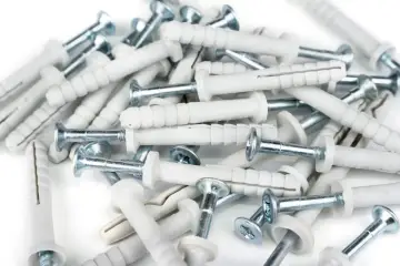 Stos białych kołków Molly z metalowymi wkrętami. Zapewniają solidny udźwig przy montażu.